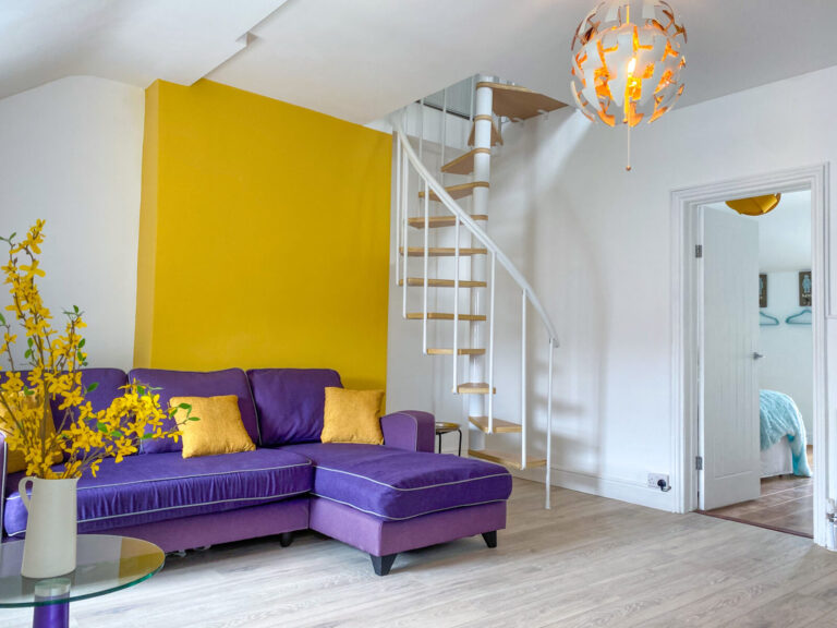 Plum velvet corner sofa and white spiral staircase in the 2-Bed Apartment