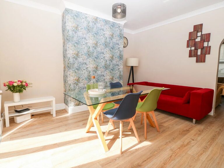 3-Bed Garden Apartment dining room with abstract feature wallpaper, green and blue chairs and red sofa